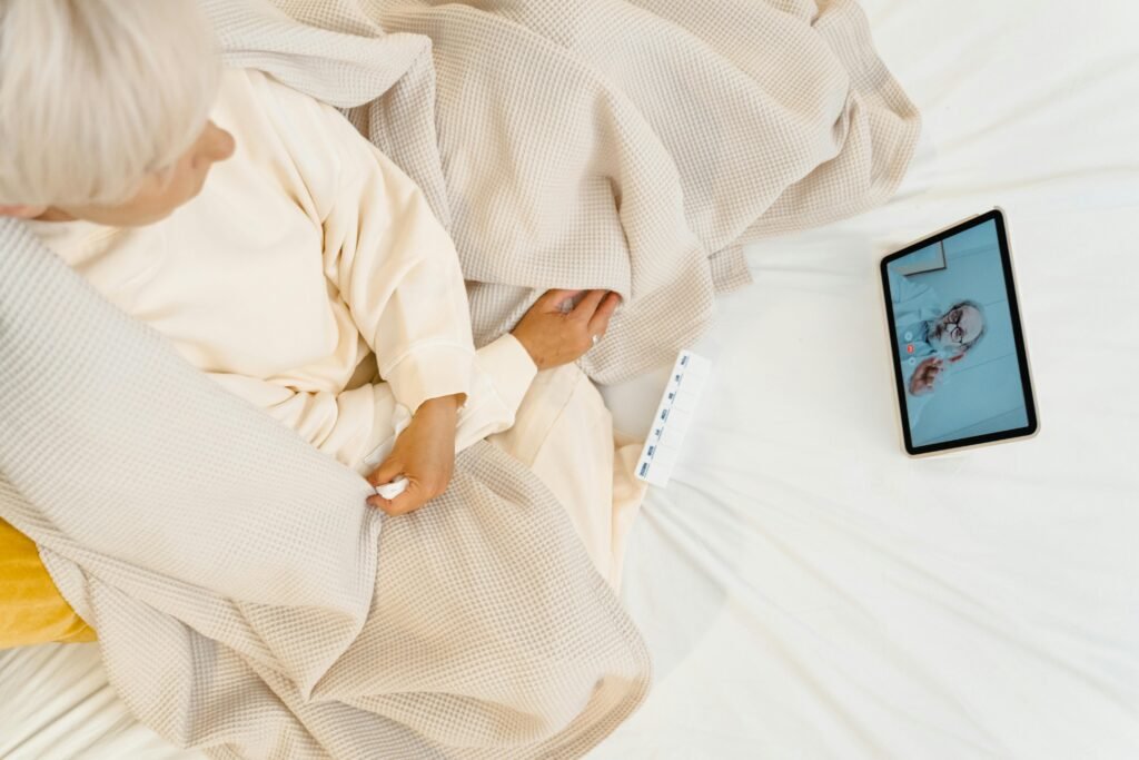 Elderly woman in bed having a video call with a doctor on a tablet, showcasing modern telehealth.
